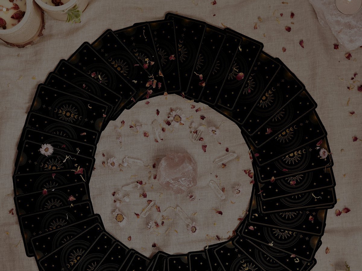 Cartas de oráculo, velas, pétalos y cristales sobre una mesa ritual elegante